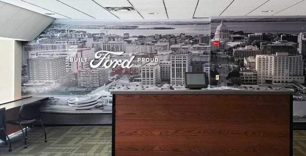 Camp Randall Luxury Suites 2 Cityscape wall mural with lettering signage "FORD", displayed behind a wooden desk.
