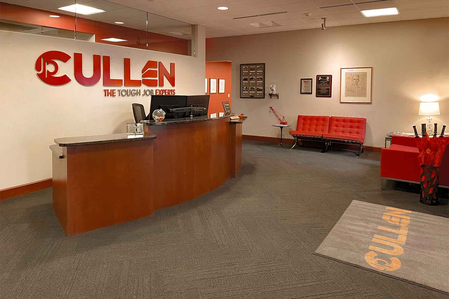 JP Cullen 7 Front desk view in JP Cullen's waiting room with chairs, a rounded desk, and the JP Cullen Logo displayed on the wall.