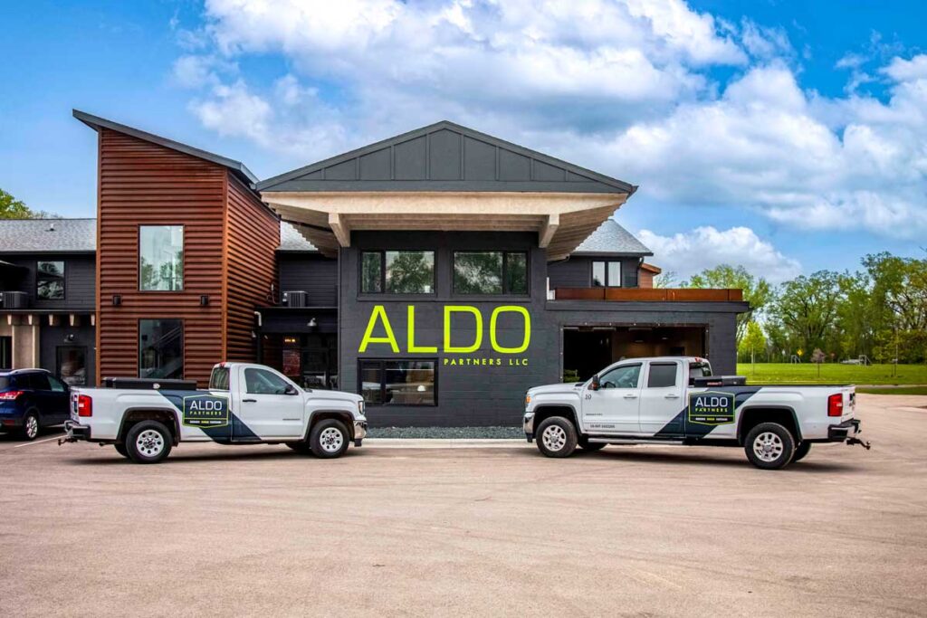 Vehicle & Fleet Wraps Portfolio 2 Two pickup trucks with custom graphics facing one another in front of a building displaying "ALDO".