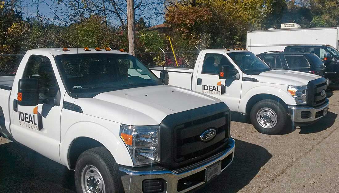 Vehicle & Fleet Wraps Portfolio 13 A row of white pickup trucks parked in a parking lot, displaying custom fleet graphics.