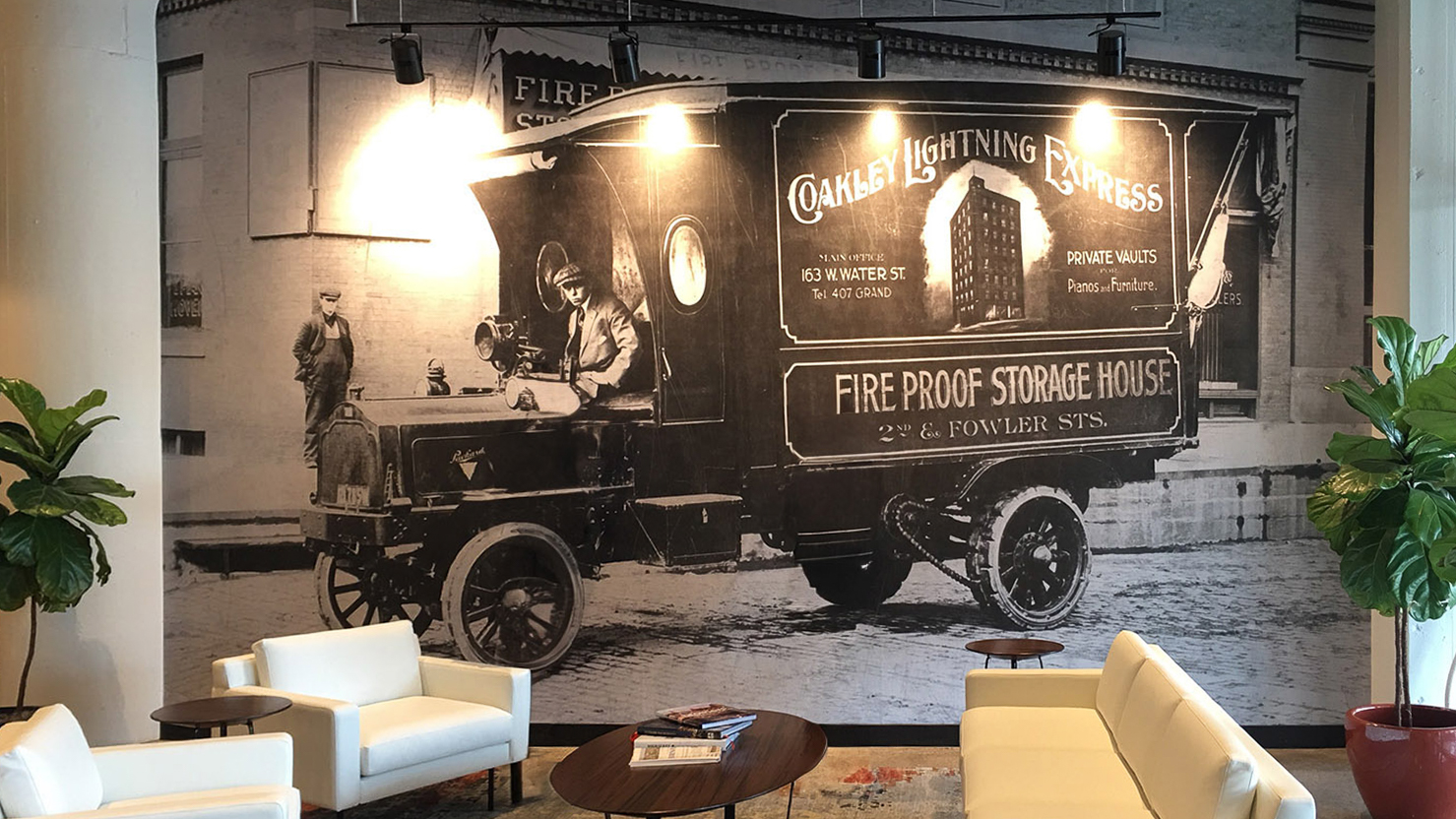 Adhesive Wall Fabric mural featuring a vintage delivery truck from Coakley Brothers, installed in a modern office lobby with white lounge chairs and plants.