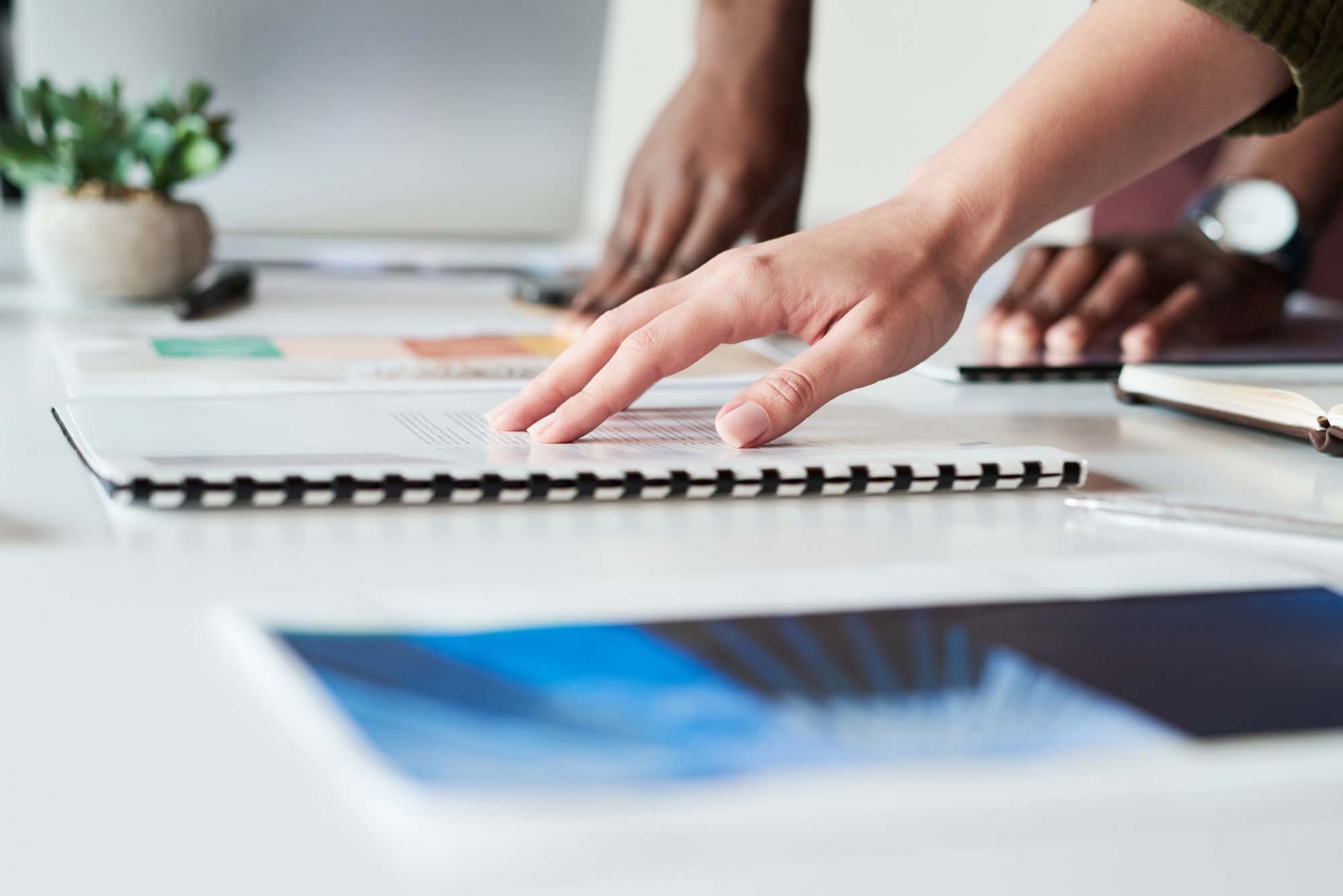 Business Printing materials on a conference table with close-up of hands reviewing spiral-bound documents and color printouts during a professional meeting.