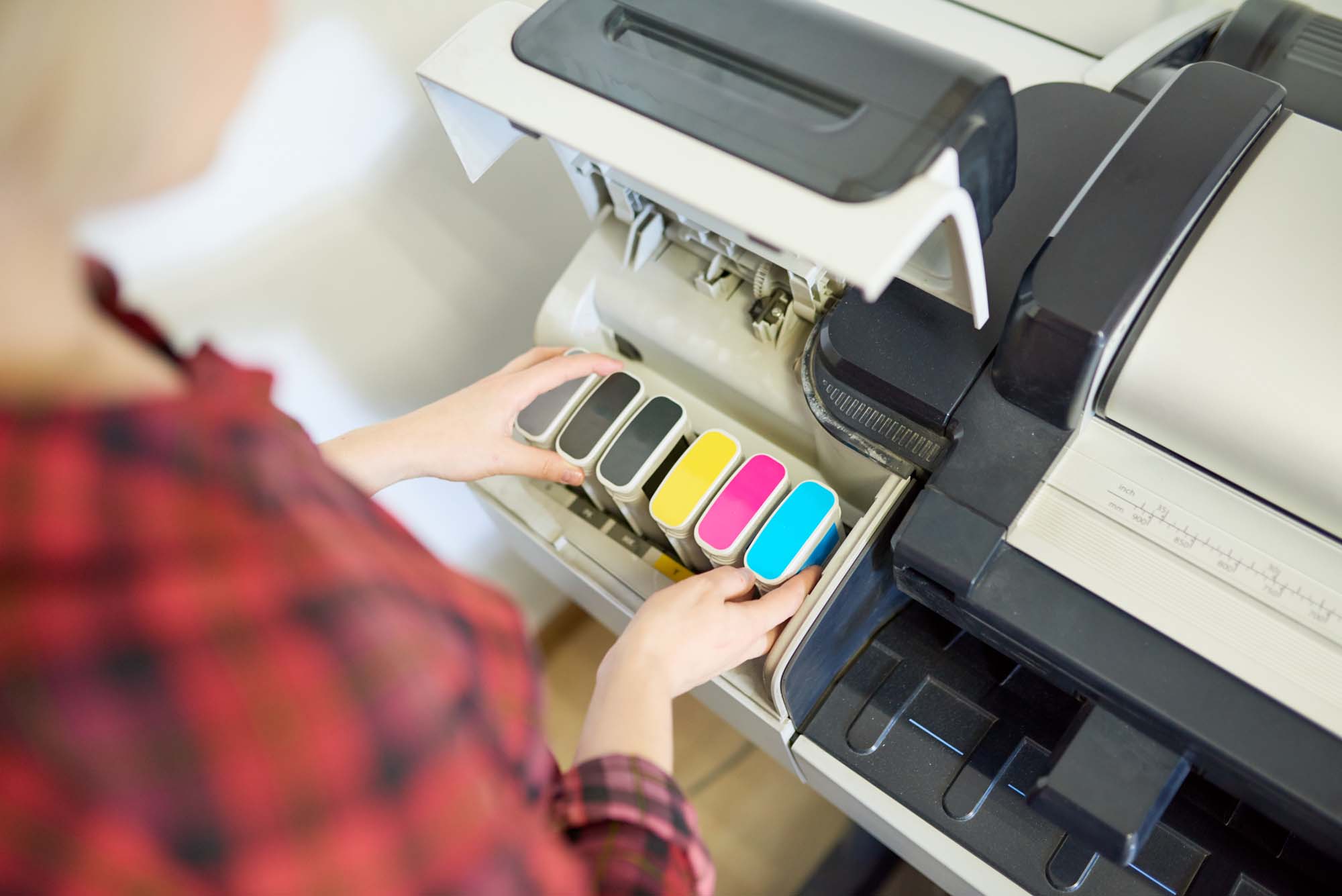 Printing Solutions Menu 6 Ink Cartridge Installation – A person installing color ink cartridges into a wide-format printer, showing cyan, magenta, yellow, and multiple shades of black.