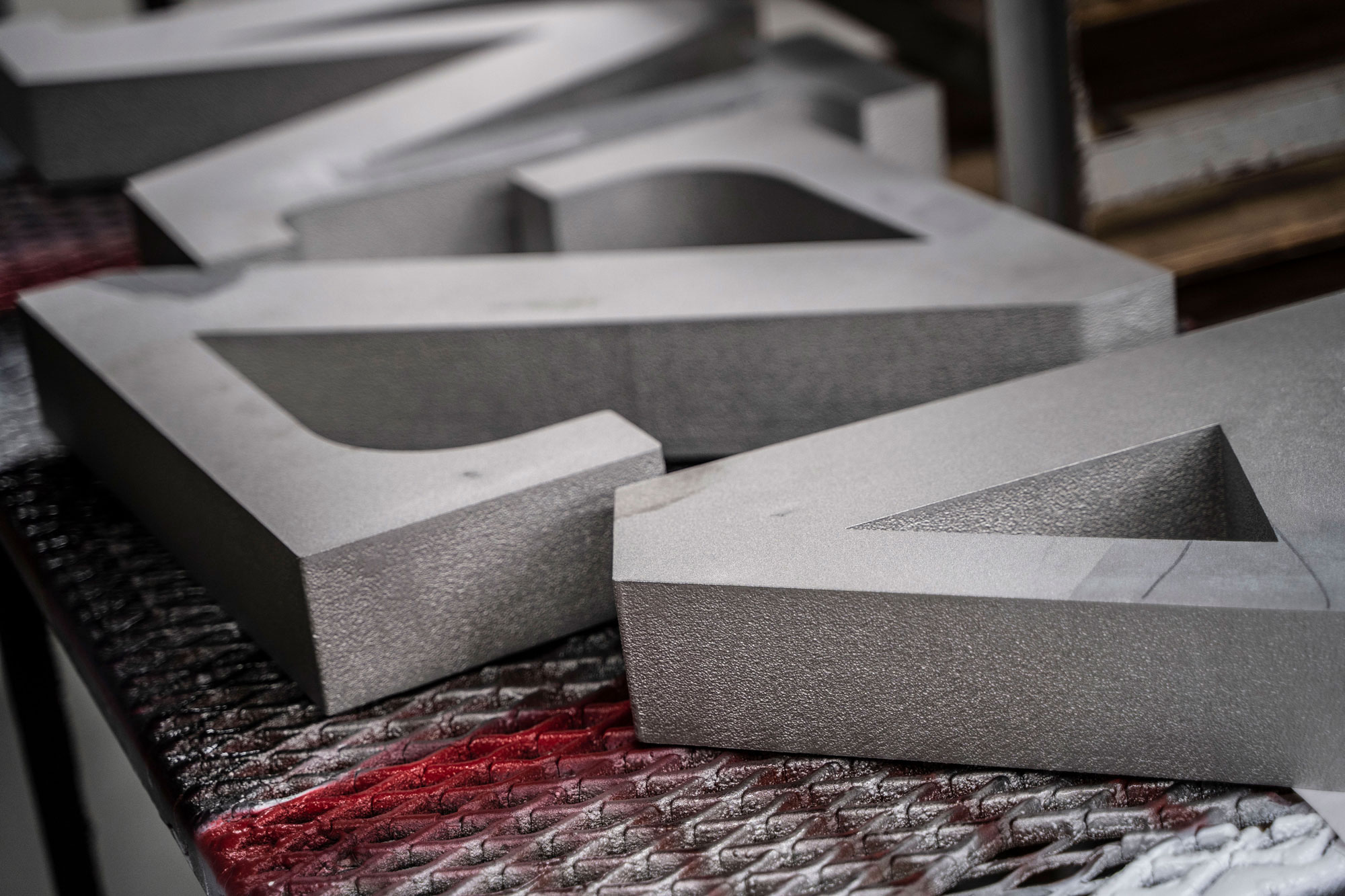 Flat Cut Metal Signage: Close-up of thick, flat cut metal letters with a textured surface, resting on a metal fabrication table during the production process.