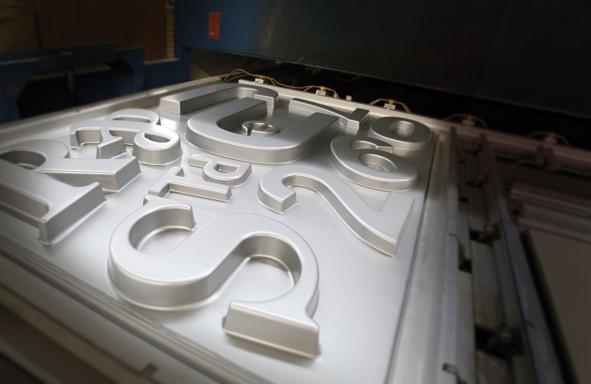 Injection Molded Plastic Signage close-up of metallic silver letters and numbers being formed in an industrial injection molding machine for dimensional signage production.