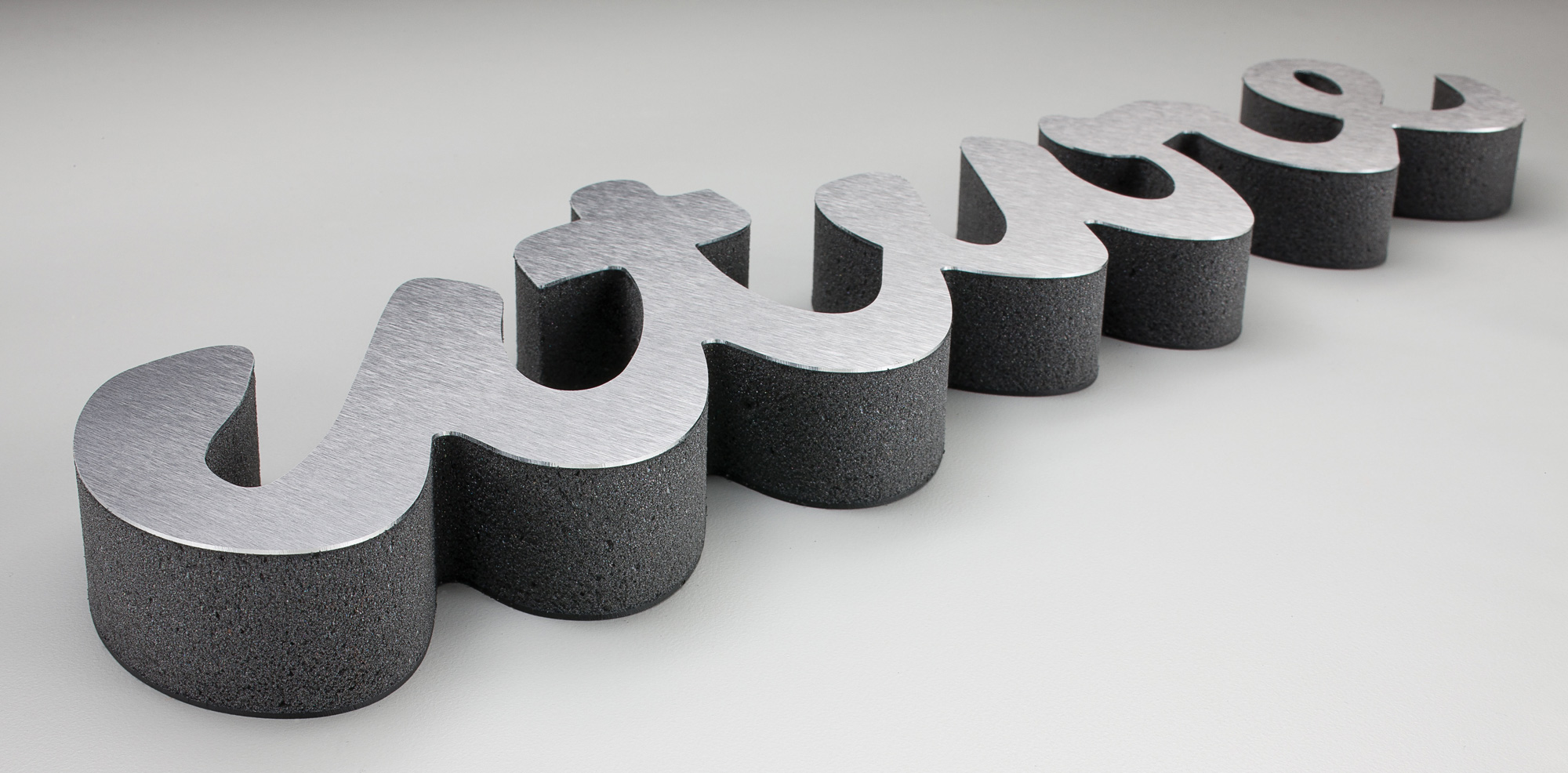 Laser Cut Dimensional Signage spelling the word “future” in a cursive script, featuring a brushed metal face and thick textured black sides, displayed on a light gray surface.