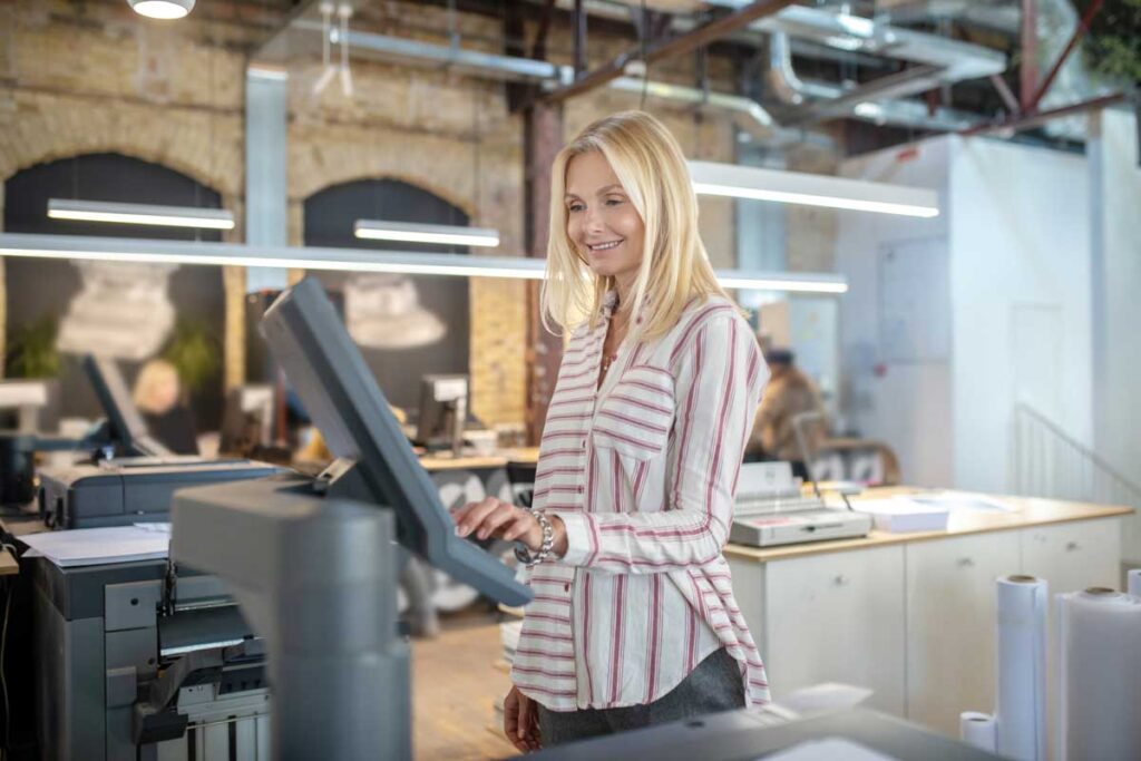 Print Tracking 1 Woman with blonde hair in a long sleeve shirt using an industrial printer.