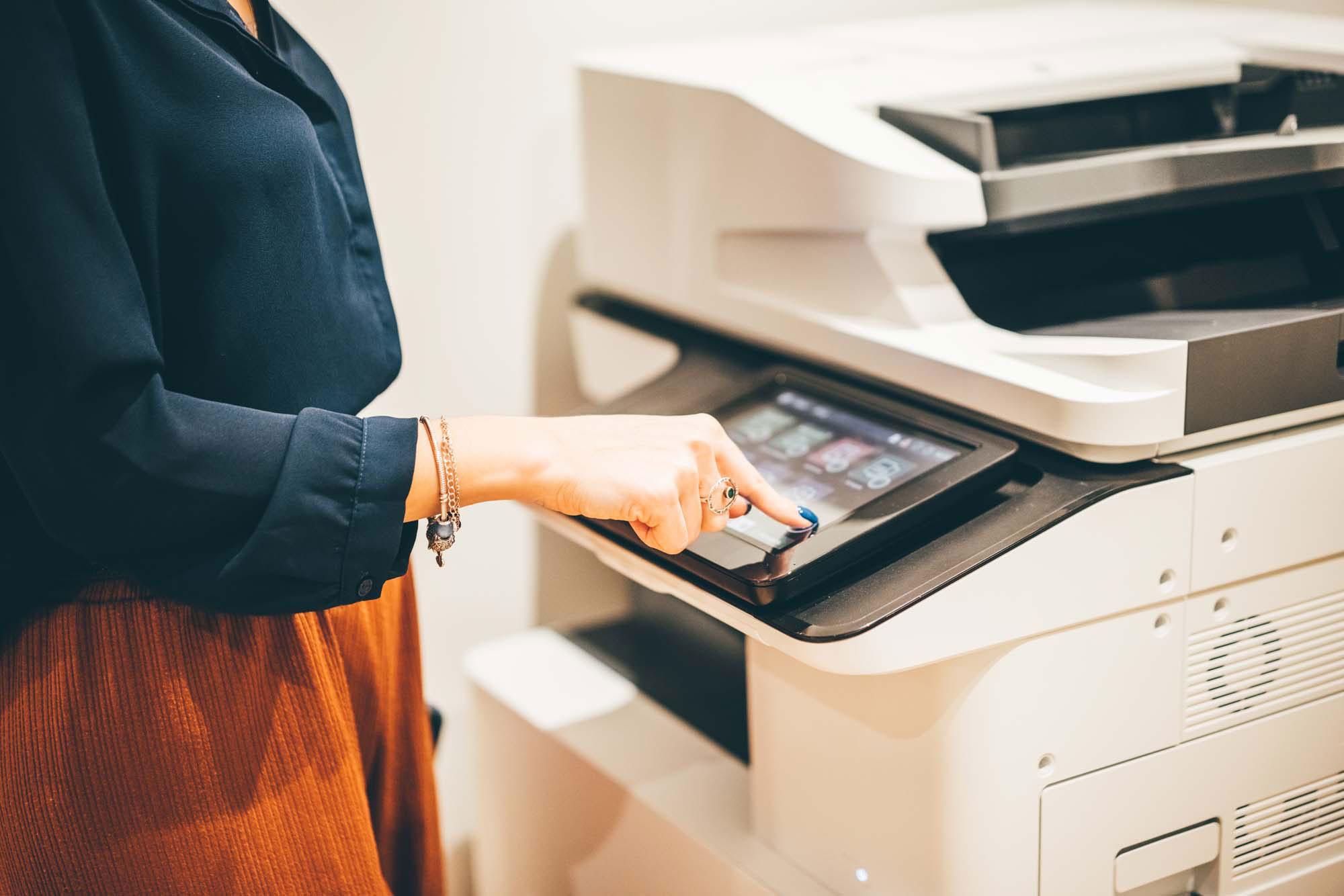 Office Printer Touchscreen – A woman operating a multifunction office printer using its touchscreen interface, wearing a navy blouse and orange pants.
