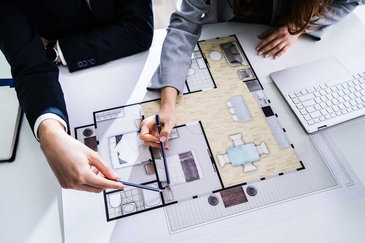 Our Story 4 Man's arm in a black suit jacket, and a woman's arm in a gray long sleeve are pointing their pens at a room diagram.