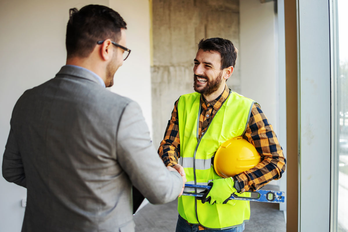 Our Story 14 A man in a gray suit shaking hands with a man in a flannel and safety vest.