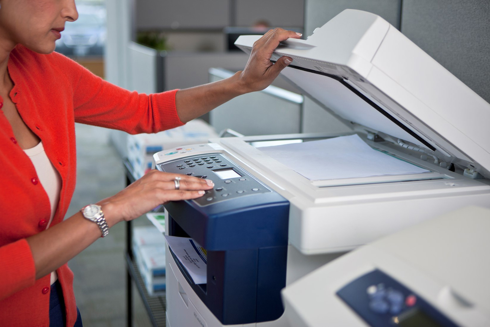 Xerox Office Printer being used by a woman in a red sweater, placing paper on the scanner bed while operating the control panel in a modern office setting.