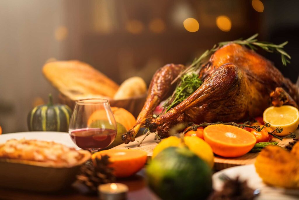 Thanksgiving Meal featuring a golden roasted turkey surrounded by citrus, vegetables, fresh bread, a glass of wine, and festive seasonal decor.