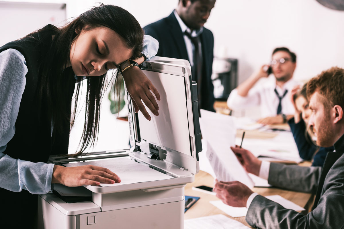 Chipped Ink Cartridges 4 Tired woman leaning over a printer.