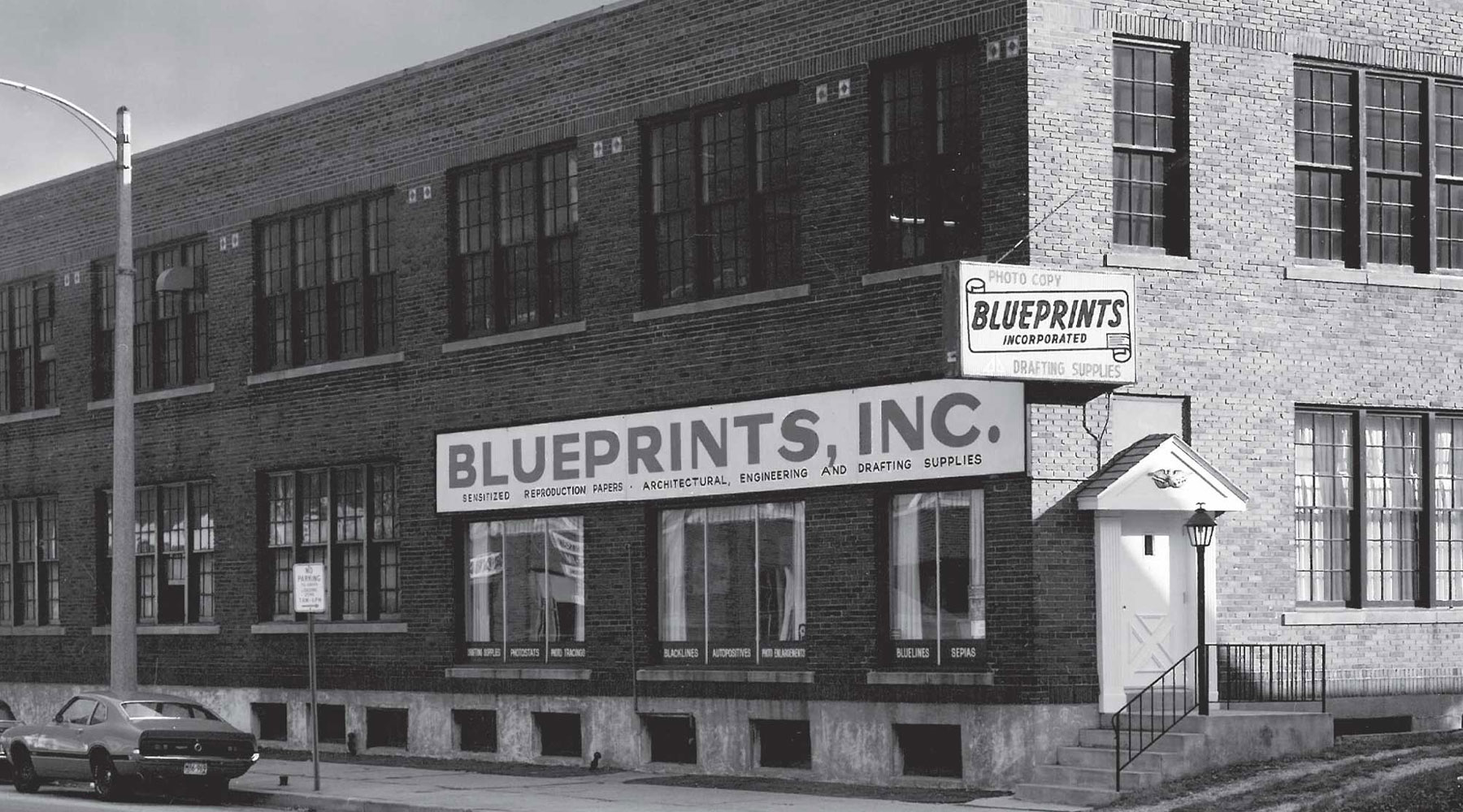 Blueprints Inc Building – A historic black-and-white photo of the original Blueprints, Inc. office featuring signage for architectural, engineering, and drafting supplies.
