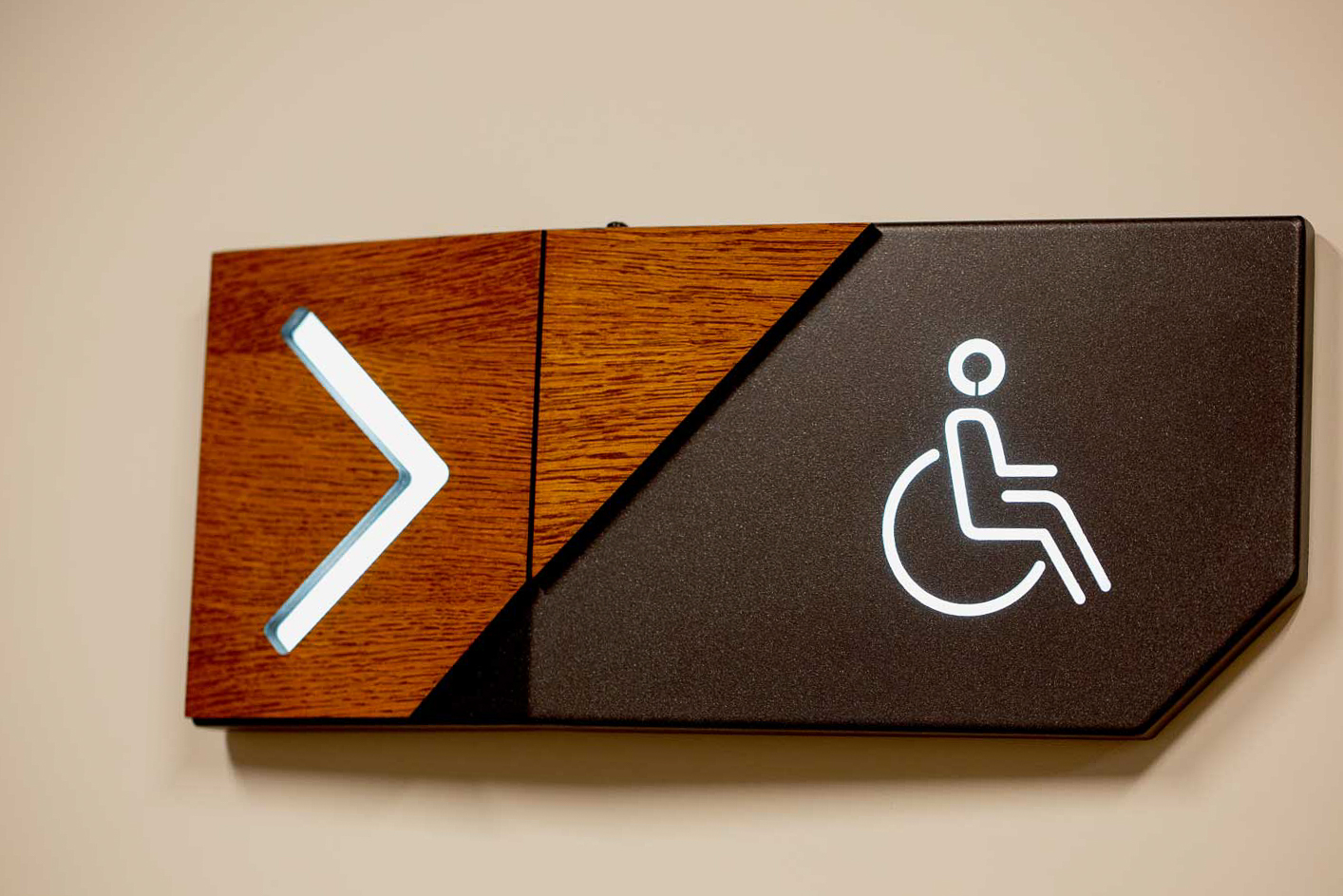 ADA and Wayfinding Signage featuring a modern, illuminated accessible icon and right arrow design with wood and matte black finishes for clear direction.