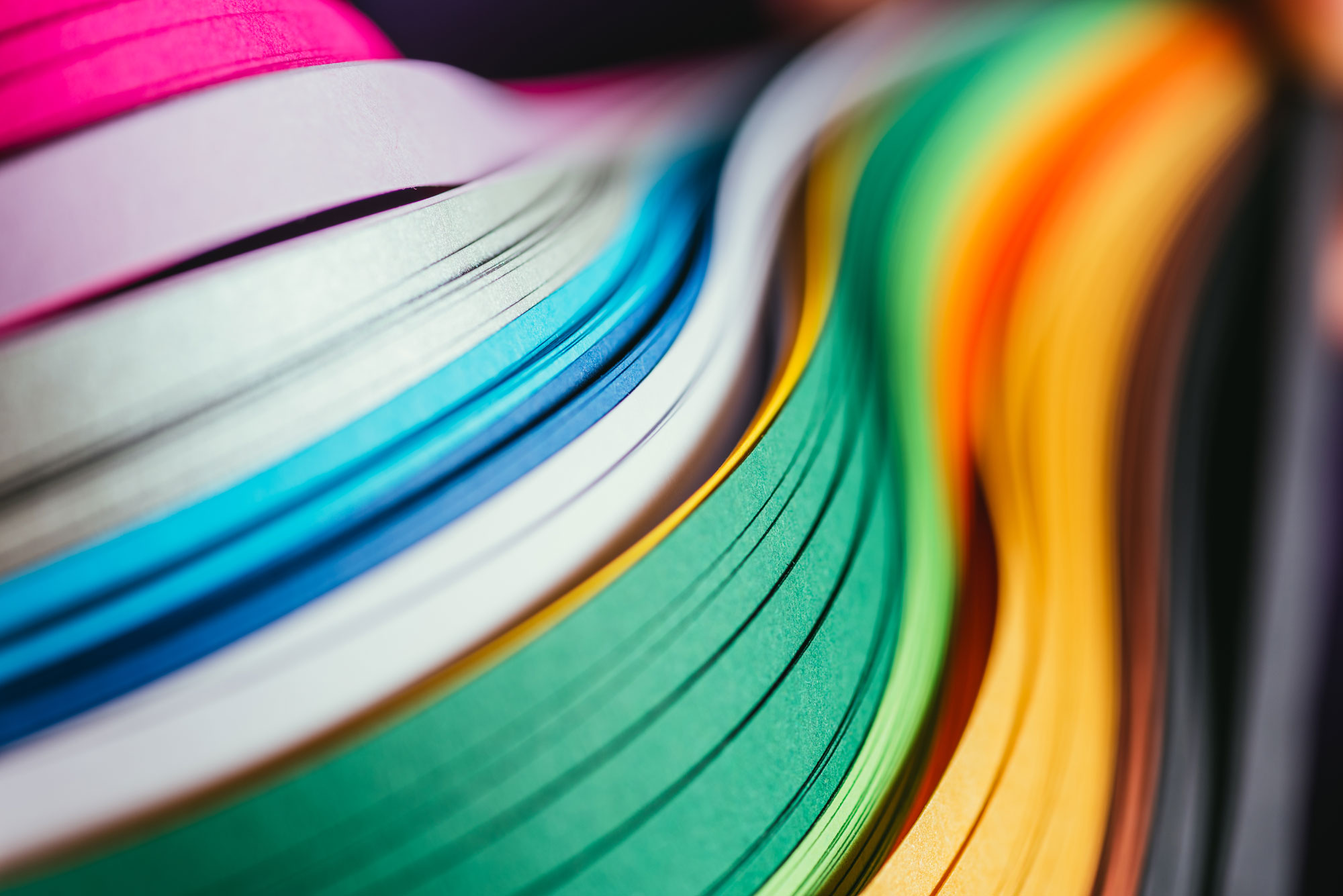 Colorful paper stacked in a smooth wave pattern, featuring vibrant hues like pink, blue, green, yellow, and orange in a high-resolution close-up.