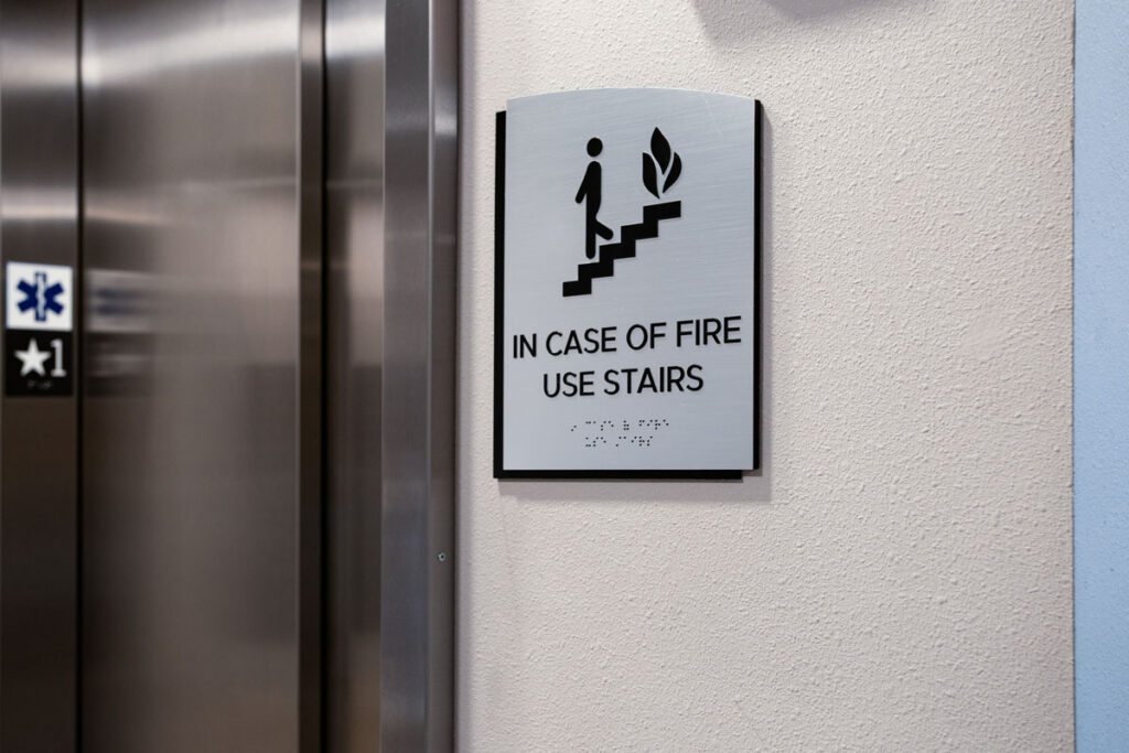 ADA Signage for Colorado Commons wall-mounted emergency instruction sign reads “In Case of Fire Use Stairs,” with ADA-compliant tactile and braille lettering.
