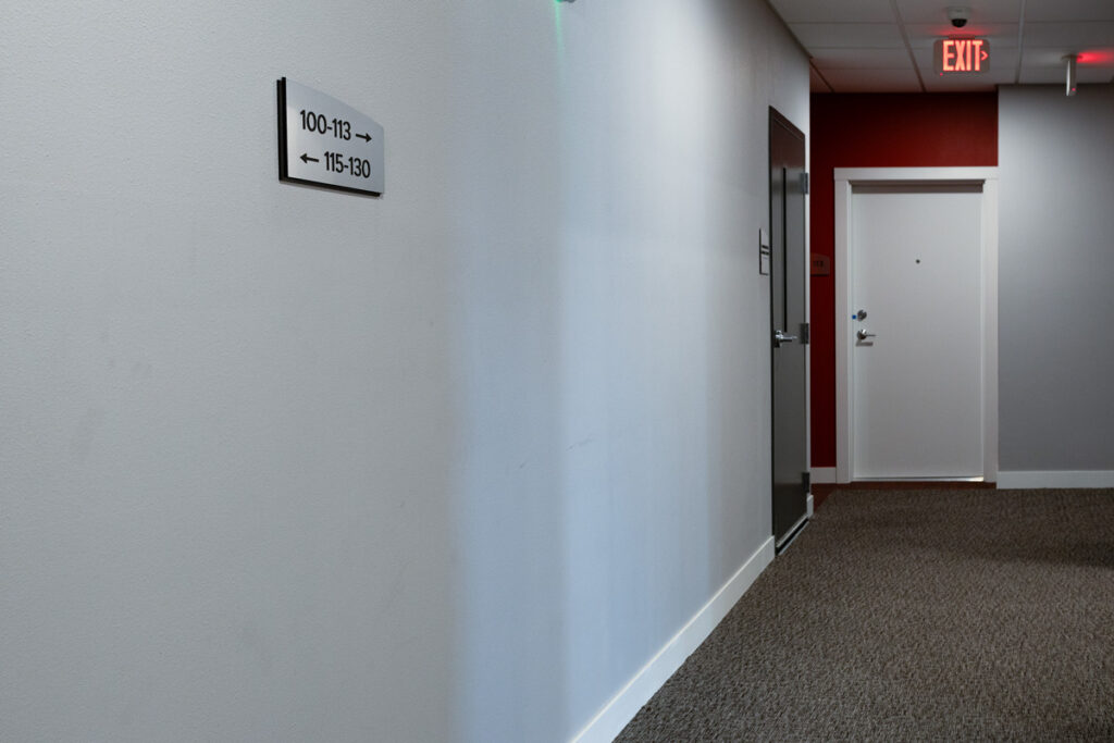 ADA Signage Colorado Commons Hallway room number sign at Colorado Commons, featuring tactile numbers and arrows for accessible wayfinding compliance.