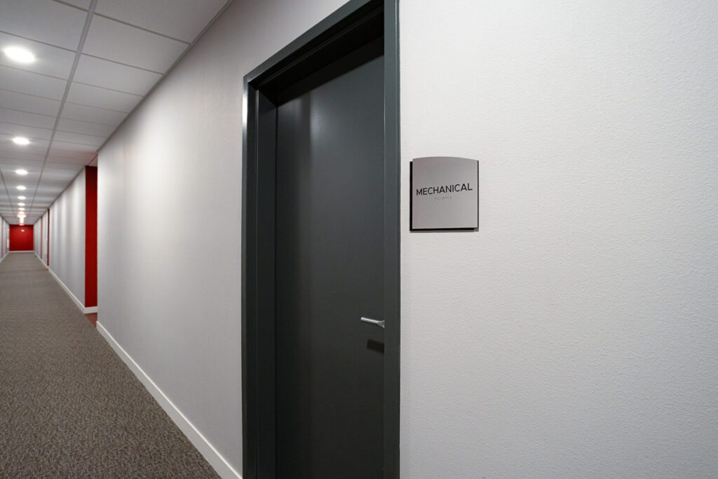 ADA Signage mechanical room door sign with tactile text and braille, mounted in a clean apartment hallway at Colorado Commons for accessibility compliance.