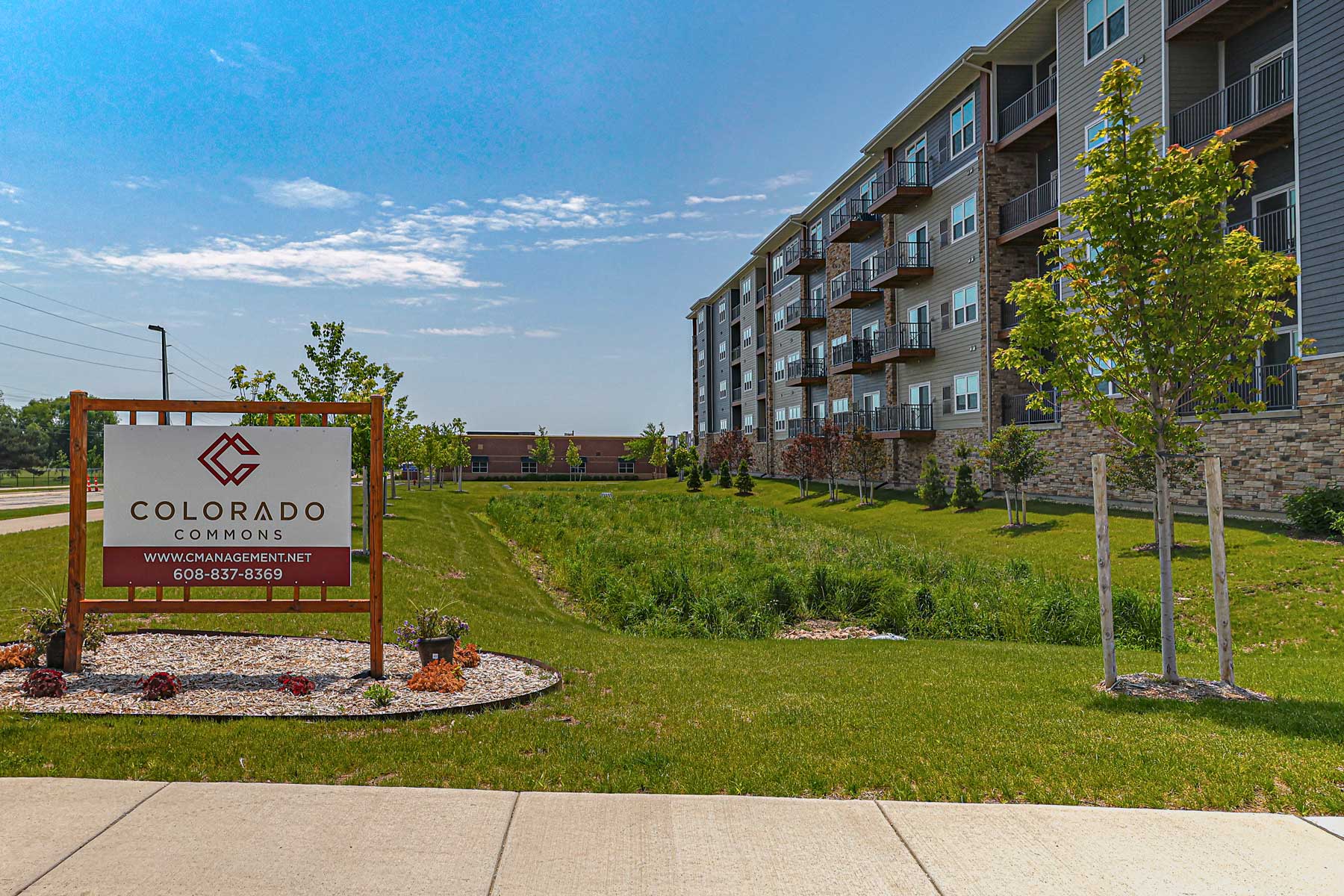 Portfolio Menu 8 Portfolio for Colorado Commons exterior signage and apartment building shown on a sunny day, highlighting landscaping and branding for the residential complex.