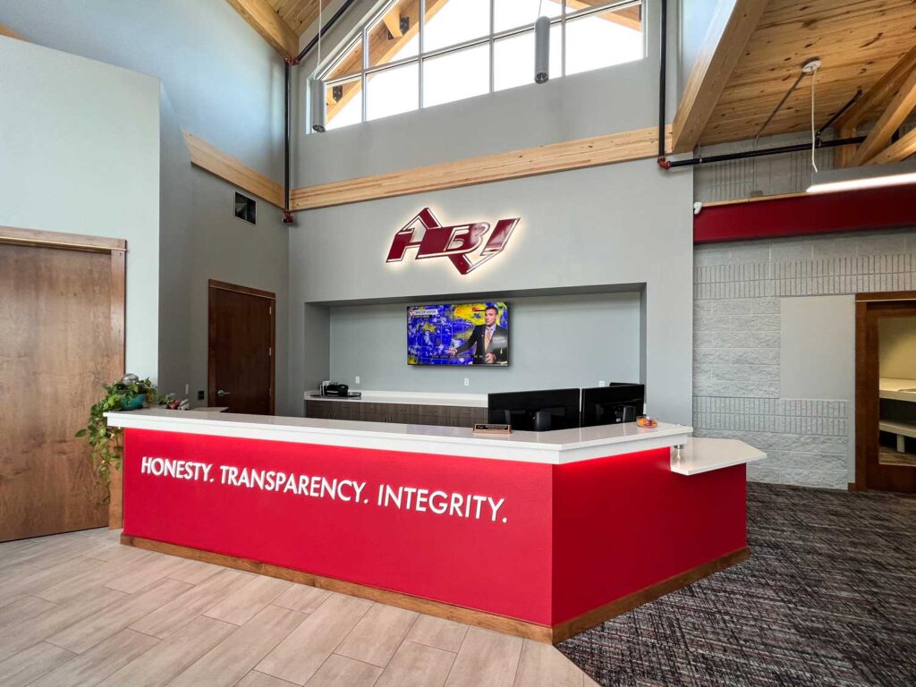 HBI Dimensional Lettering displayed on a bright red reception desk with the words “HONESTY. TRANSPARENCY. INTEGRITY.” in a modern, high-ceiling lobby.