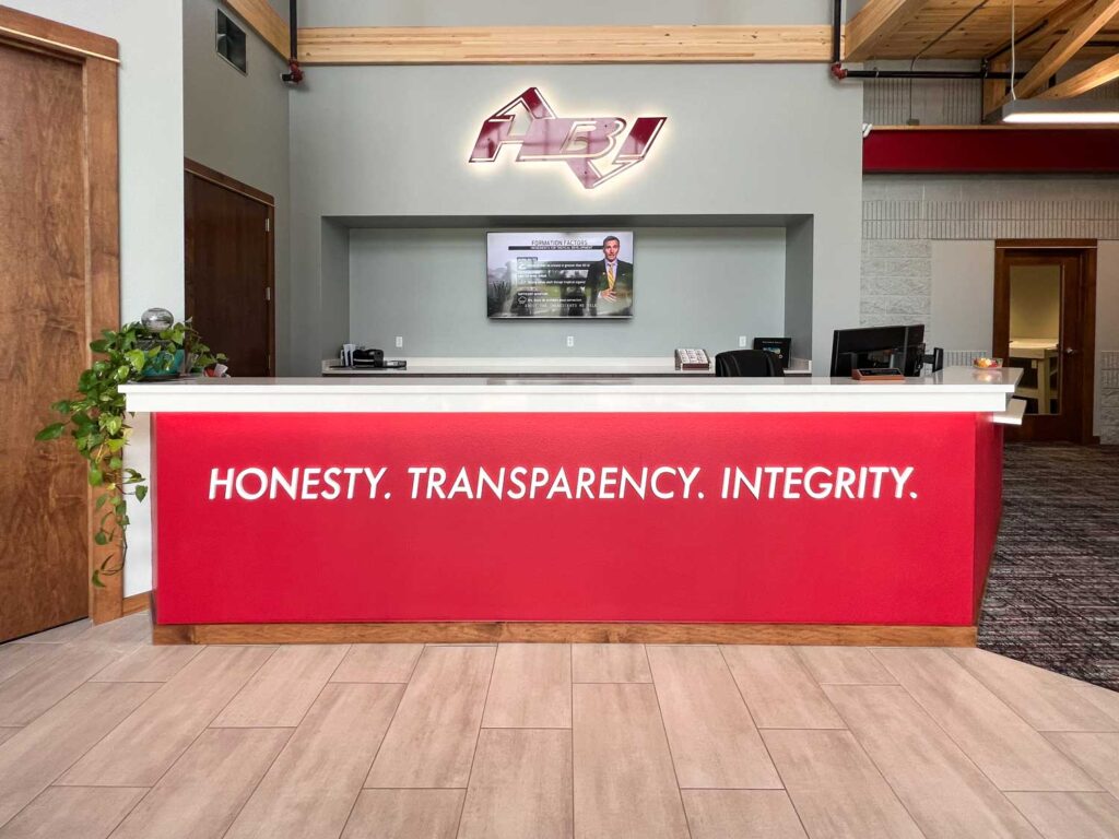 HBI Dimensional Lettering on a red reception desk reading “HONESTY. TRANSPARENCY. INTEGRITY.” in a modern lobby with clean lines and wood accents.