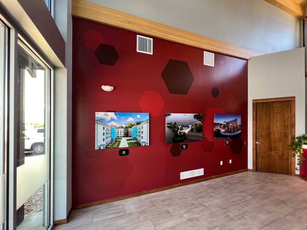 HBI Adhesive Wall Wrap with deep red tones and hexagon patterns, featuring mounted project photos in a modern office lobby with high ceilings and natural light.