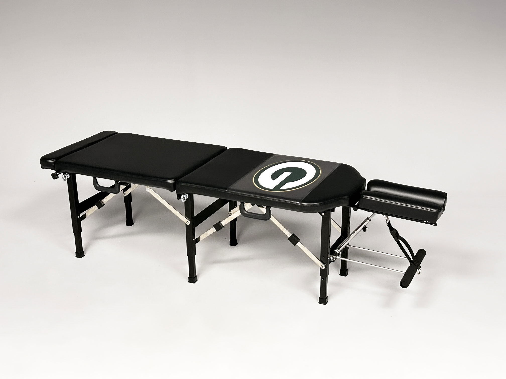 Portfolio Menu 6 Thuli Tables custom black chiropractic table featuring the Green Bay Packers “G” logo, complete with adjustable headrest and foldable legs.