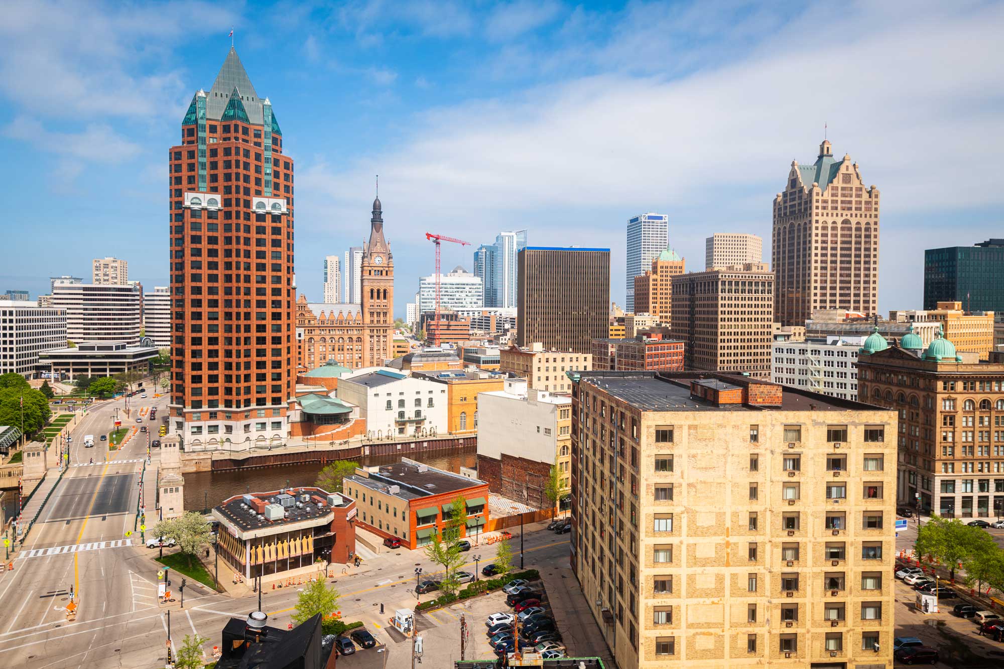 Milwaukee, WI downtown skyline on a bright summer day featuring a mix of historic and modern architecture, with prominent buildings like the Milwaukee City Hall and 100 East Wisconsin under a blue sky.